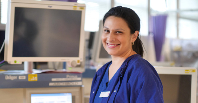 Nurse in scrubs is smiling next to anaesthetic equipment in hospital