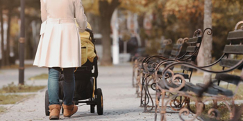 Woman walking while pushing a pram through a park in autumn. 