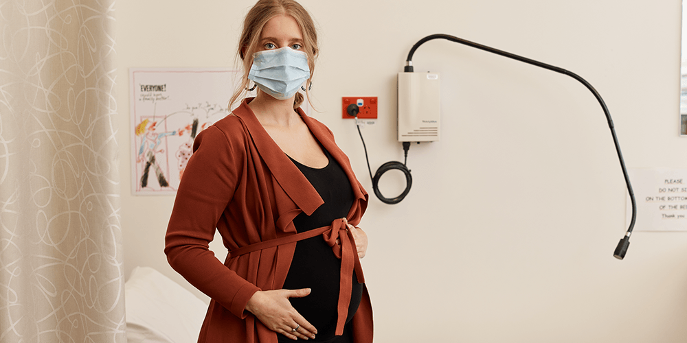 Pregnant woman in a hospital consultation room, wearing a face mask.