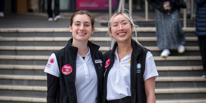 Two volunteers in uniform smiling on the front steps of the Women's 