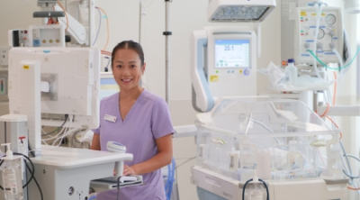Nurse in scrubs is surrounded by NICU medical equipment in hospital