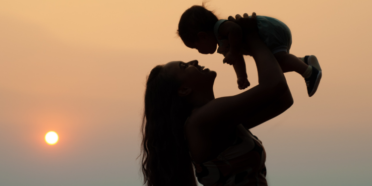 Silhouette of a woman holding up a baby. 