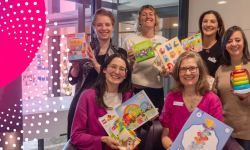 Six staff members of the First Thousand Days Clinic are holding up toys and smiling into the camera.  
